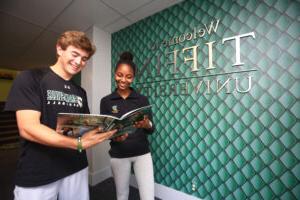 two students standing in the welcome center in front of the tiffin university sign